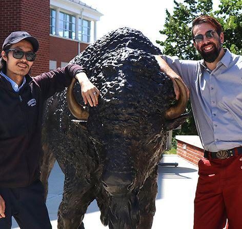 Charles and Dave, Nichols College's eSports Coaches standing next to Nichols College's bison statue, Thunder.
